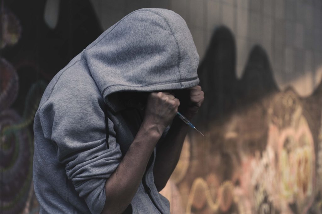 A man addicted to opioids, holding a syringe and wearing a hoodie.