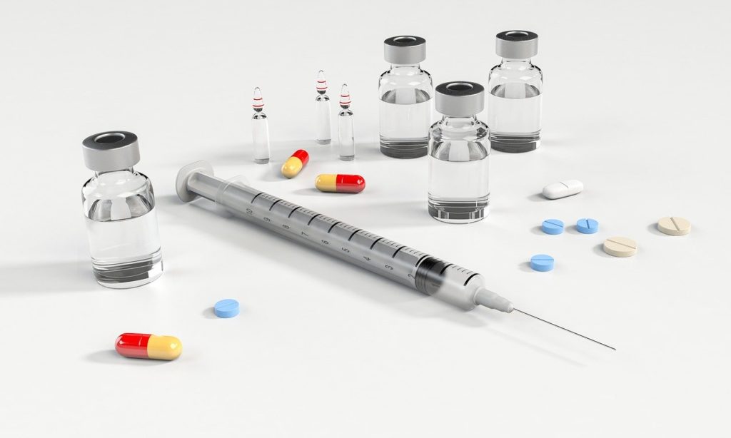 syringe, pills and capsules on white desk